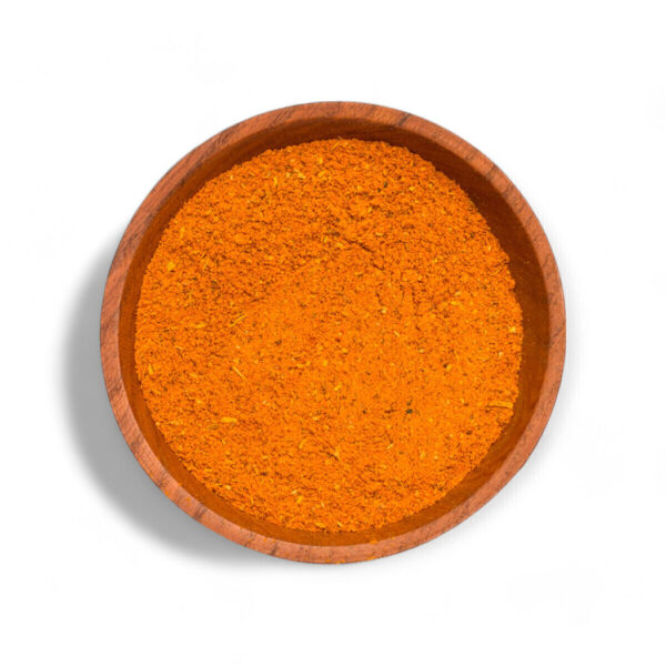 Cuenco de madera con curry en polvo de color anaranjado sobre fondo blanco.